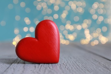 Red decorative heart on grey wooden table against blurred lights, closeup