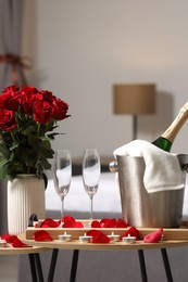 Honeymoon. Sparkling wine, glasses and bouquet of roses on wooden table in room