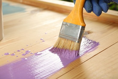 Photo of Worker applying violet paint onto wooden surface, closeup