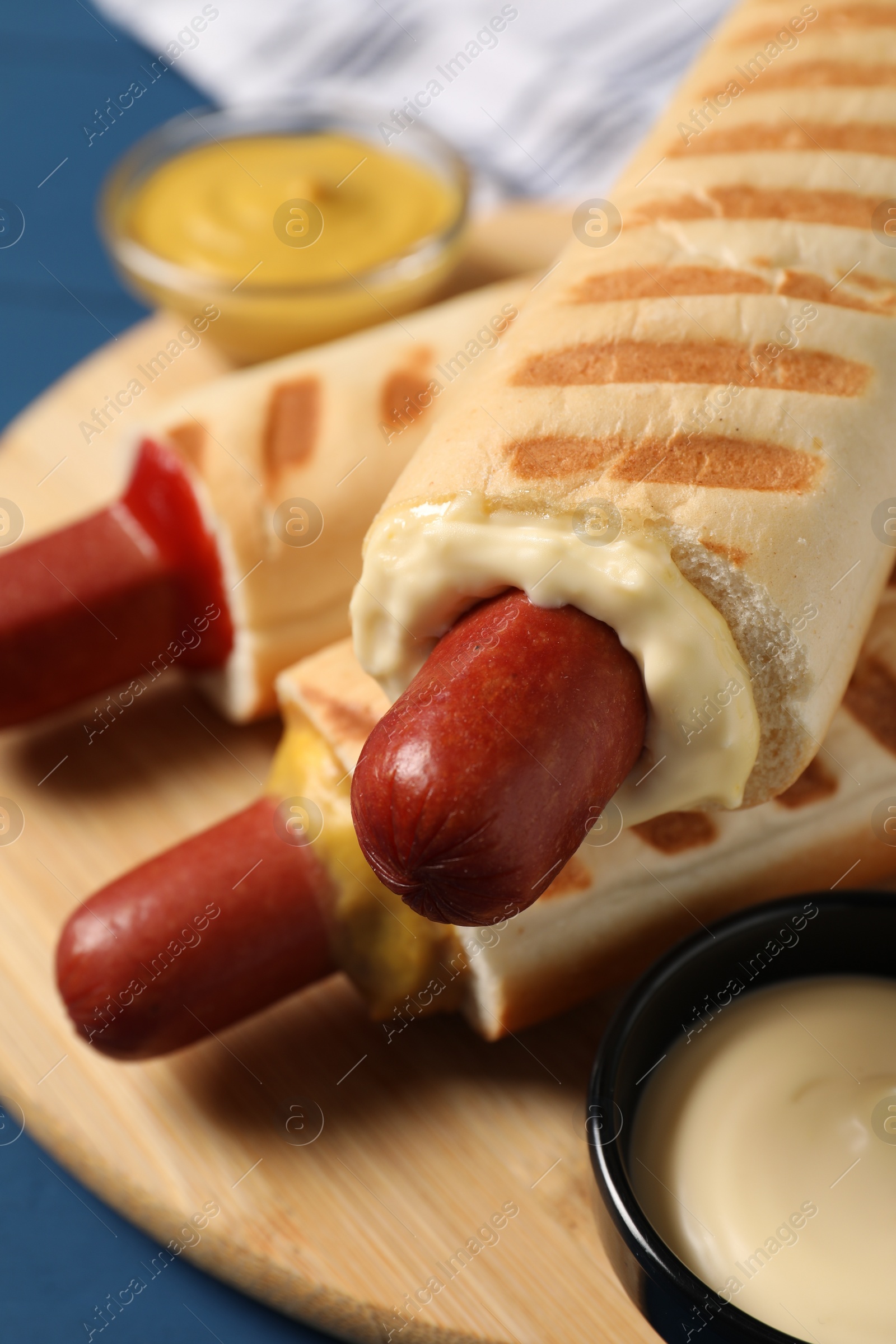 Photo of Tasty french hot dogs and dip sauces on wooden board, closeup