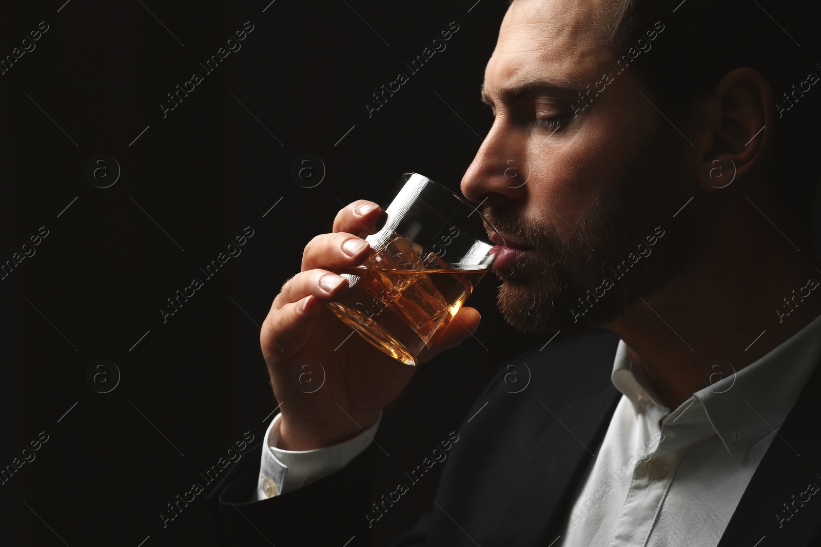 Photo of Man in suit drinking whiskey on black background