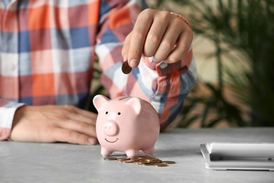 Photo of Man putting coin into piggy bank at grey marble table, closeup. Money savings
