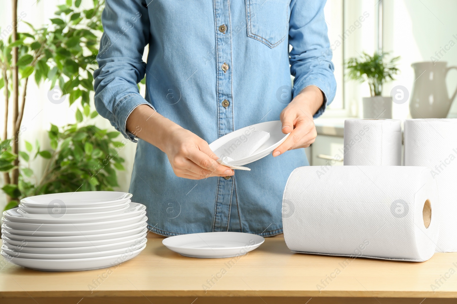 Photo of Woman wiping ceramic plate with paper towel indoors, closeup