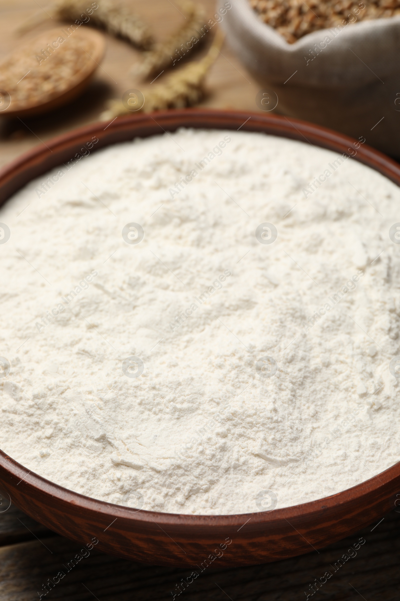 Photo of Wheat flour in bowl on wooden table, closeup