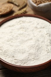 Photo of Wheat flour in bowl on wooden table, closeup