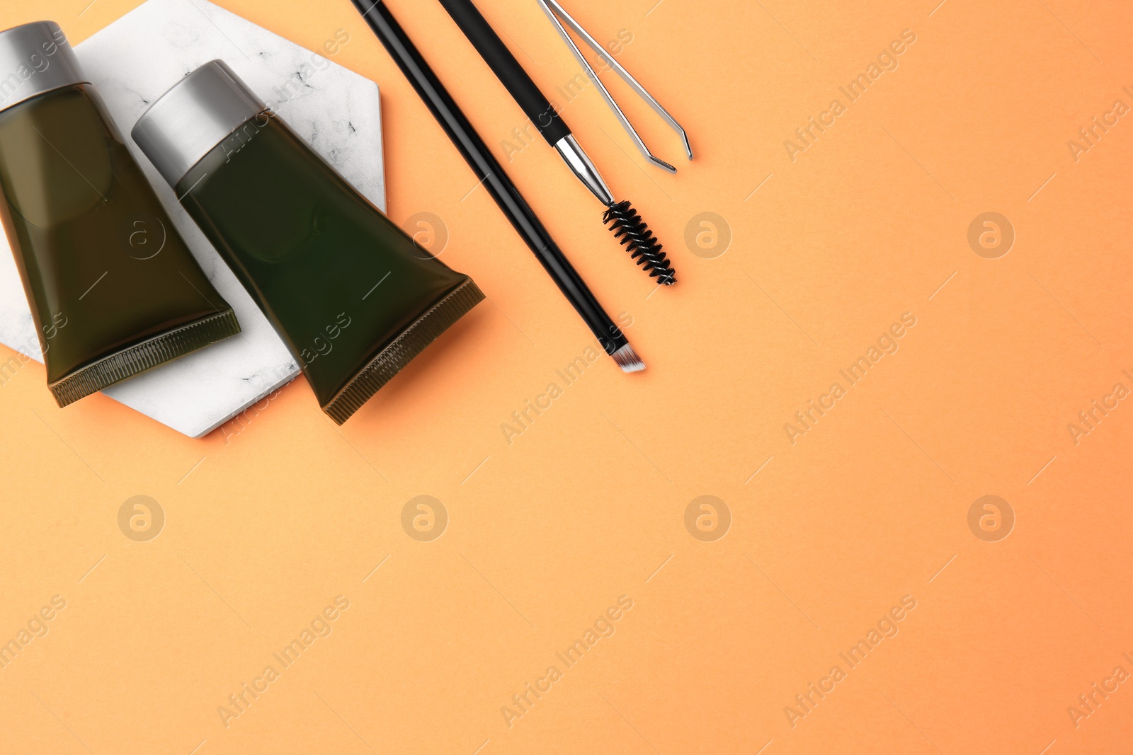 Photo of Flat lay composition with eyebrow henna, professional tools and cosmetic products on orange background, space for text