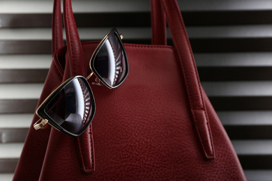 Stylish woman's bag and sunglasses on striped background, closeup