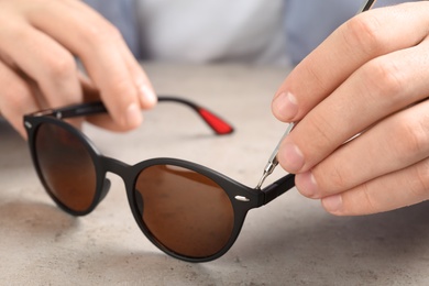 Handyman repairing sunglasses with screwdriver at grey table, closeup
