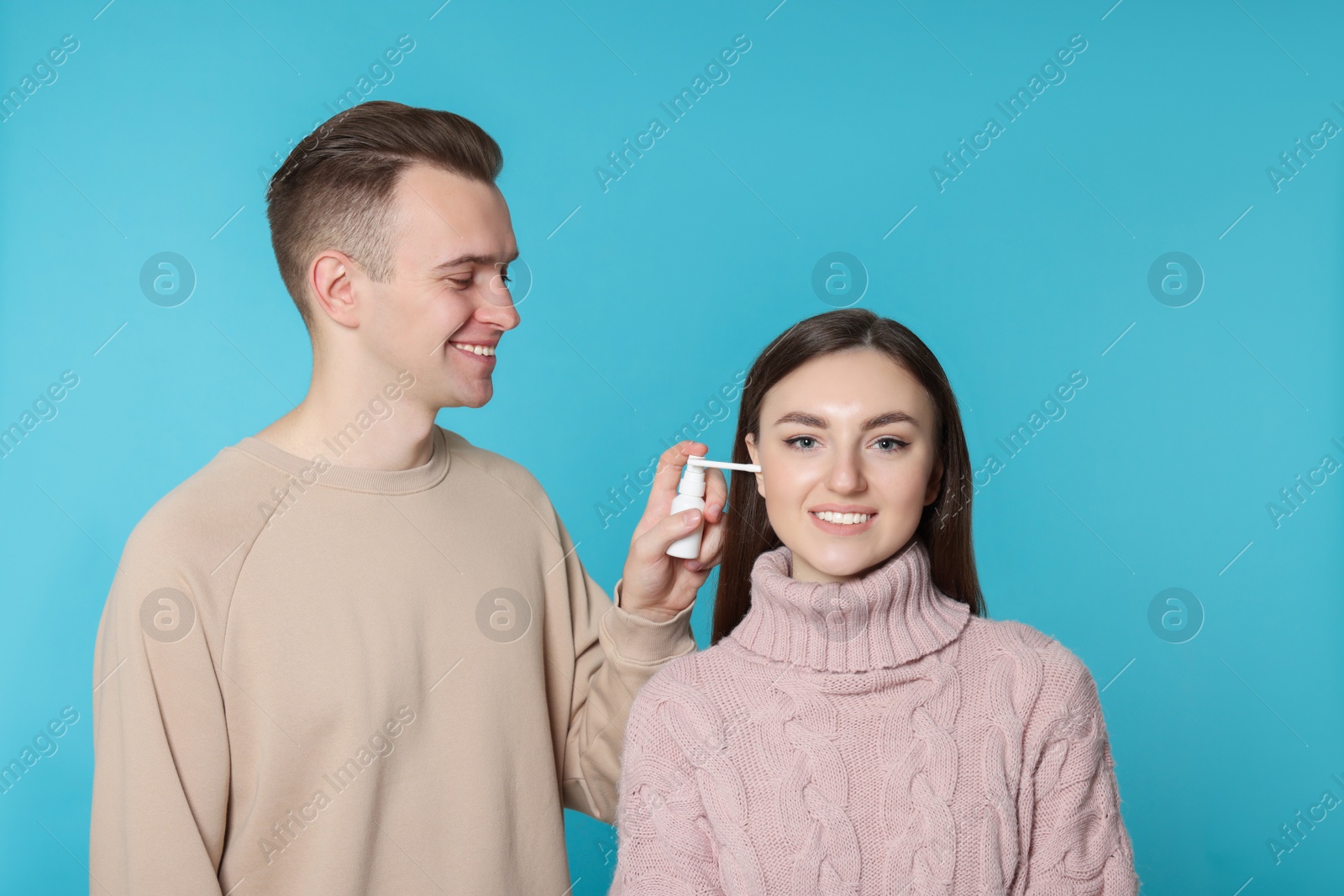 Photo of Man spraying medication into woman`s ear on light blue background