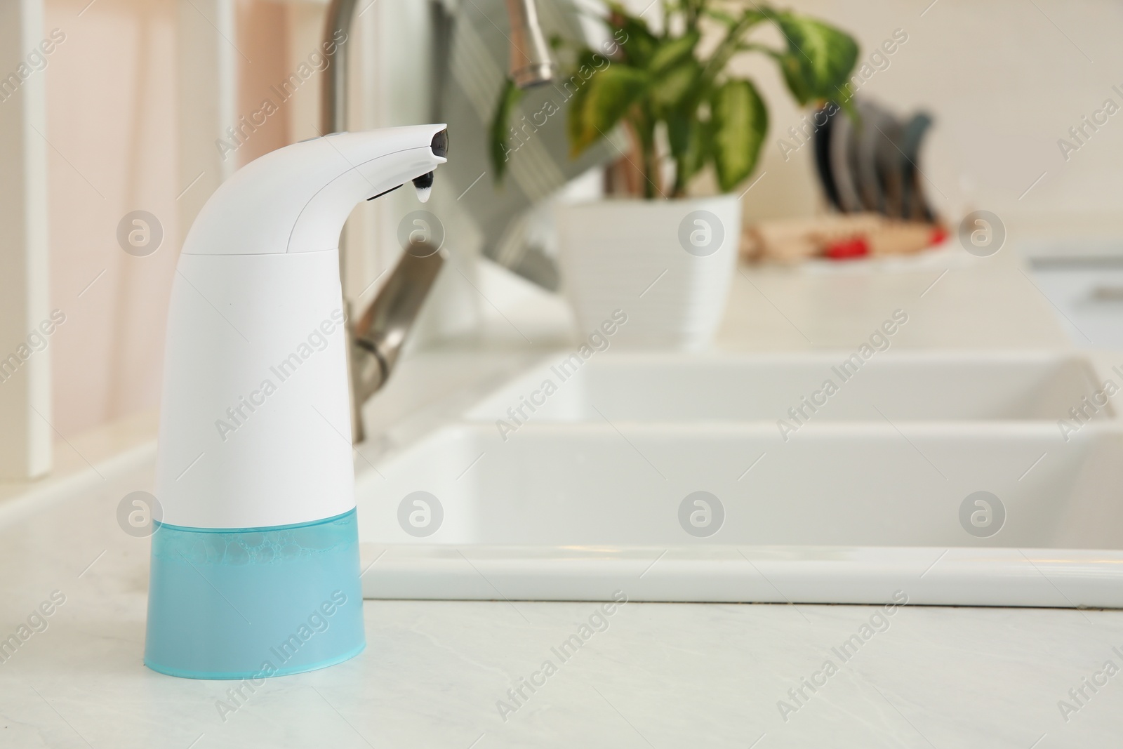 Photo of Modern automatic soap dispenser on countertop in kitchen. Space for text