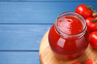 Photo of Organic ketchup in jar and fresh tomatoes on blue wooden table, space for text. Tomato sauce