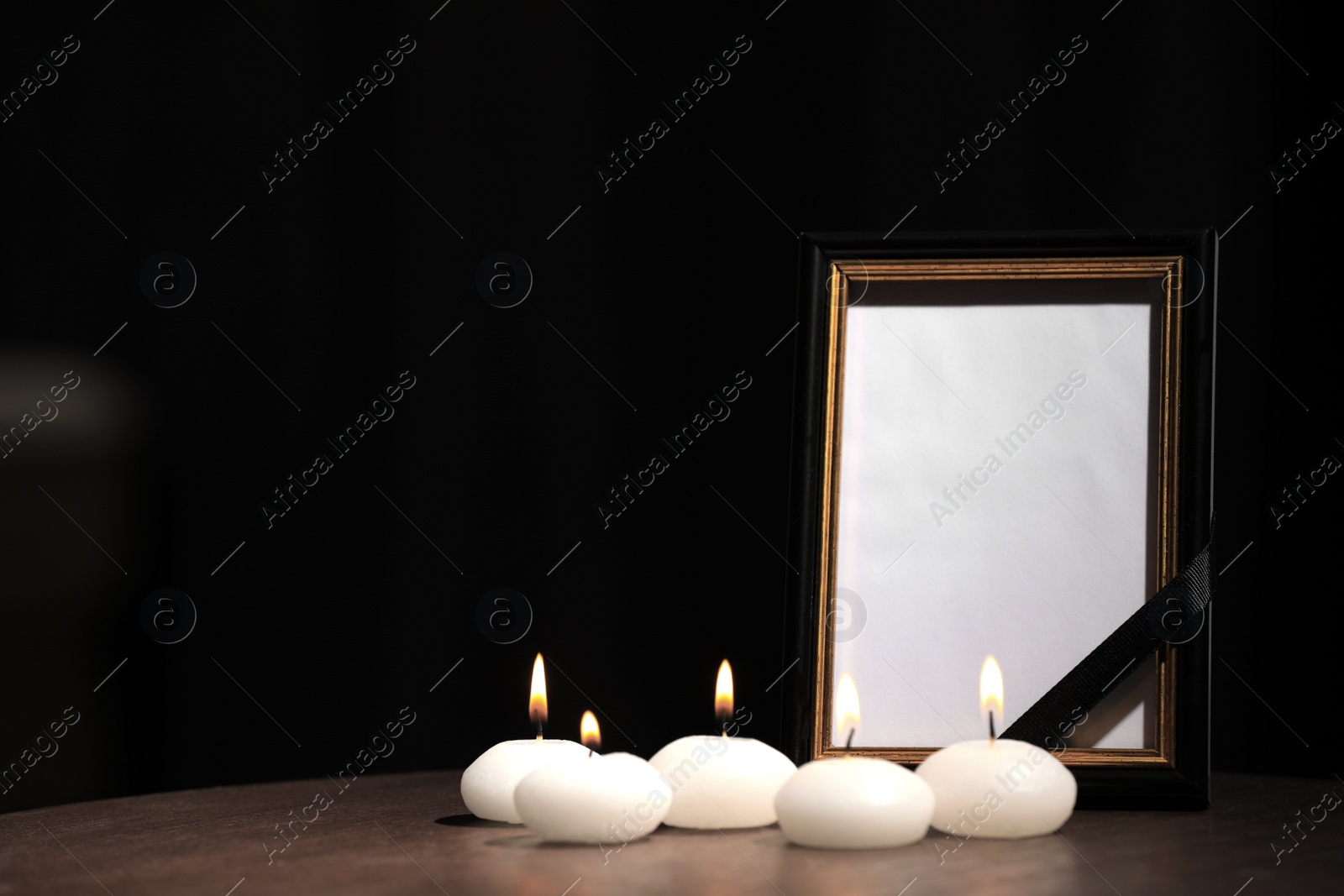 Photo of Funeral photo frame with black ribbon and candles on wooden table indoors. Space for design