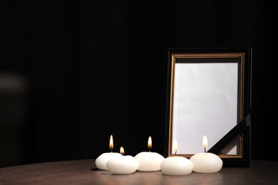 Funeral photo frame with black ribbon and candles on wooden table indoors. Space for design