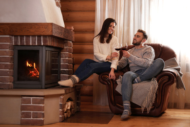 Photo of Happy couple with wine near fireplace indoors. Winter vacation