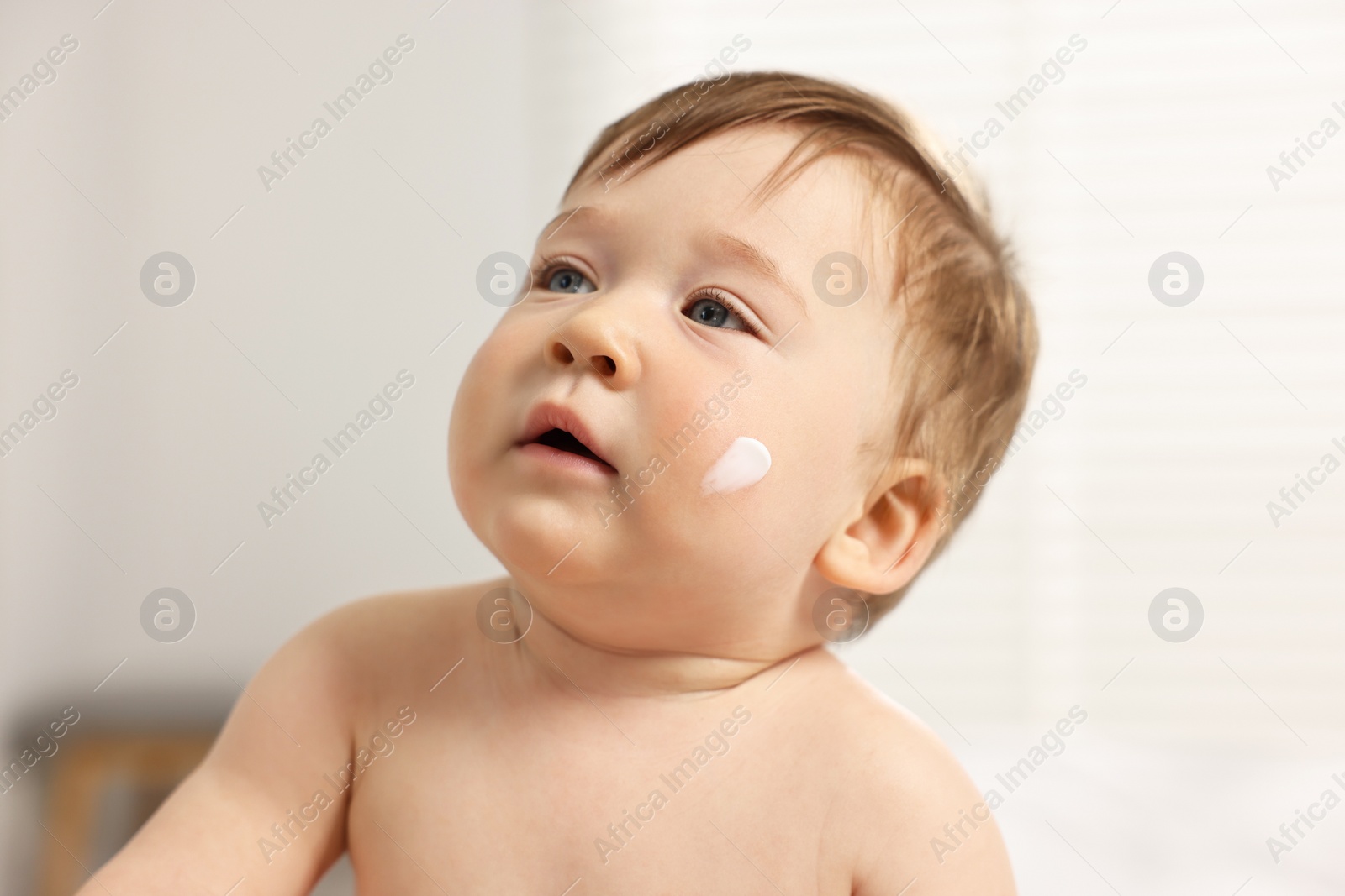 Photo of Cute little baby with moisturizing cream on face indoors