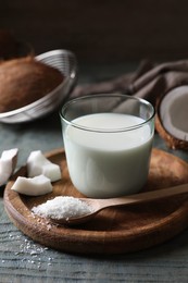 Photo of Glass of delicious coconut milk, spoon with flakes and nuts on wooden table