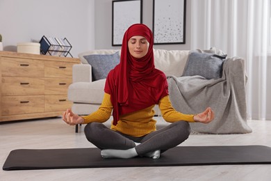 Photo of Muslim woman in hijab meditating on fitness mat at home