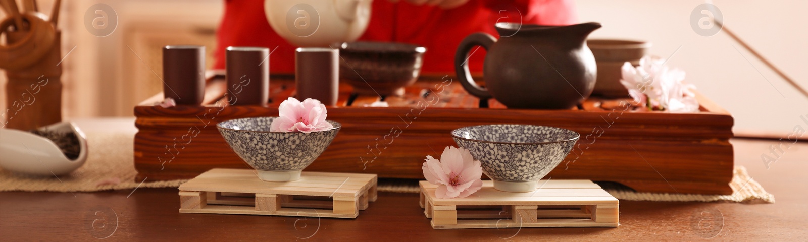 Image of Closeup view of master conducting traditional ceremony at table indoors, focus on cups and sakura flowers. Banner design