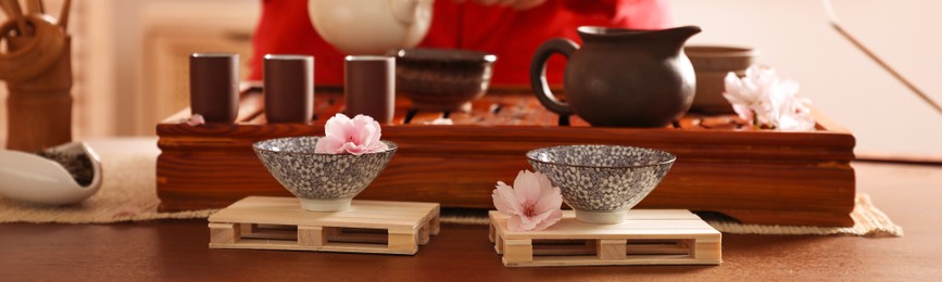 Image of Closeup view of master conducting traditional ceremony at table indoors, focus on cups and sakura flowers. Banner design