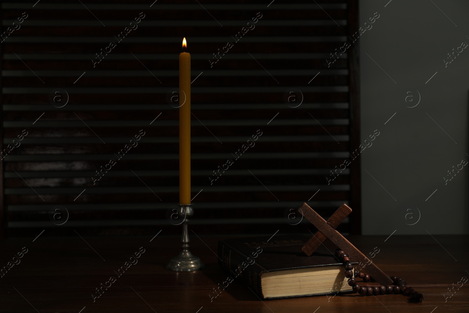 Photo of Church candle, Bible, cross and rosary beads on wooden table