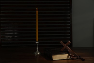 Church candle, Bible, cross and rosary beads on wooden table