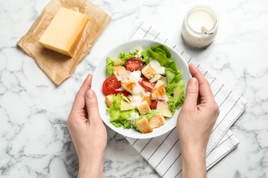 Photo of Woman with bowl of delicious fresh Caesar salad at white marble table, top view