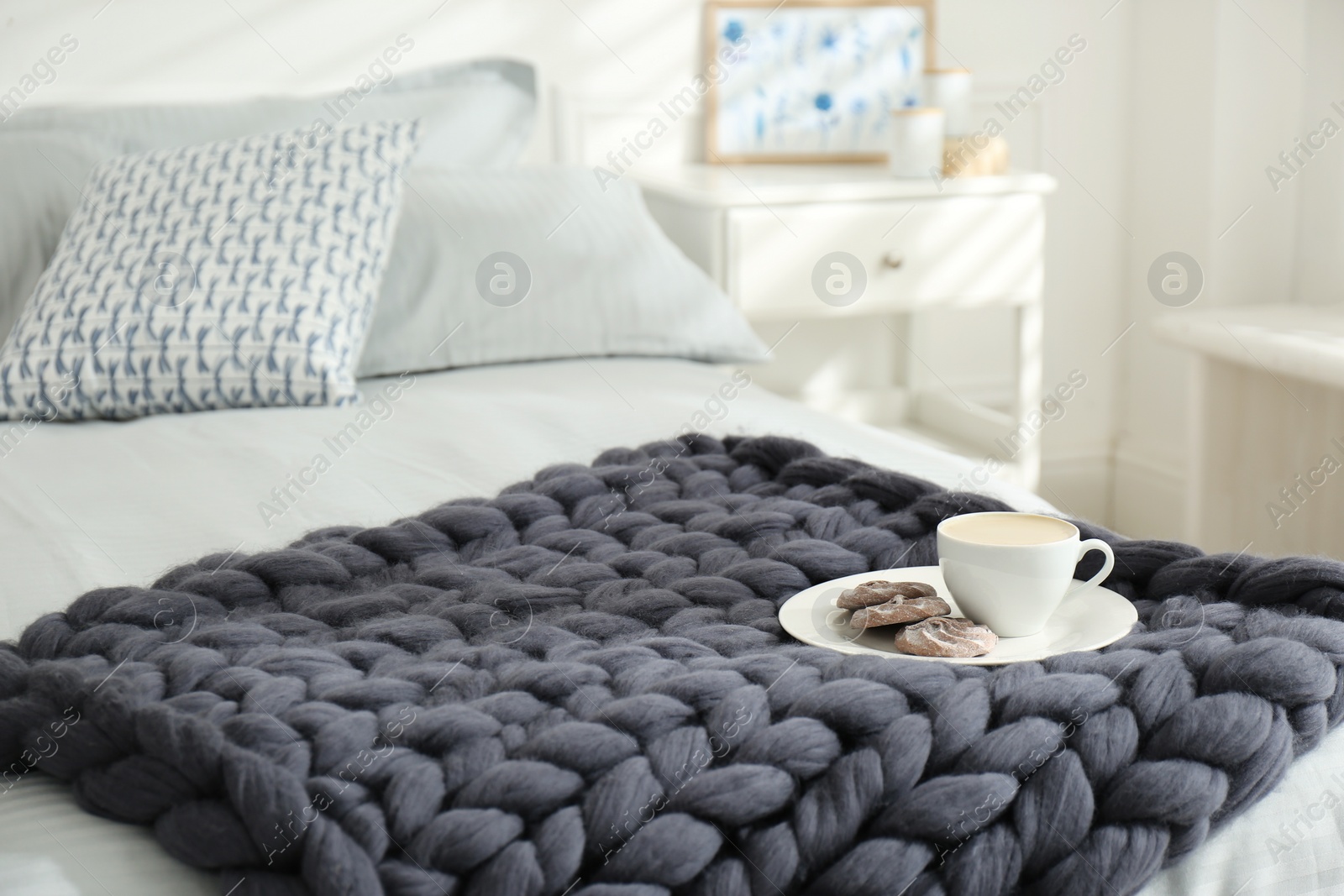 Photo of Cup of coffee with cookies on knitted merino wool plaid in bedroom, space for text
