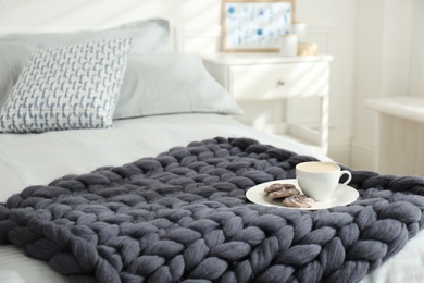 Photo of Cup of coffee with cookies on knitted merino wool plaid in bedroom, space for text