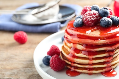 Delicious pancakes with fresh berries and syrup on wooden table, closeup