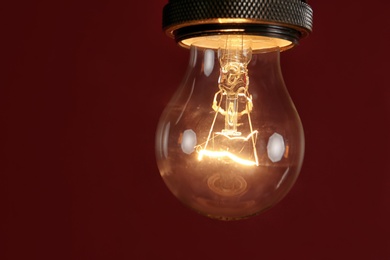 Pendant lamp with light bulb against dark red background, space for text