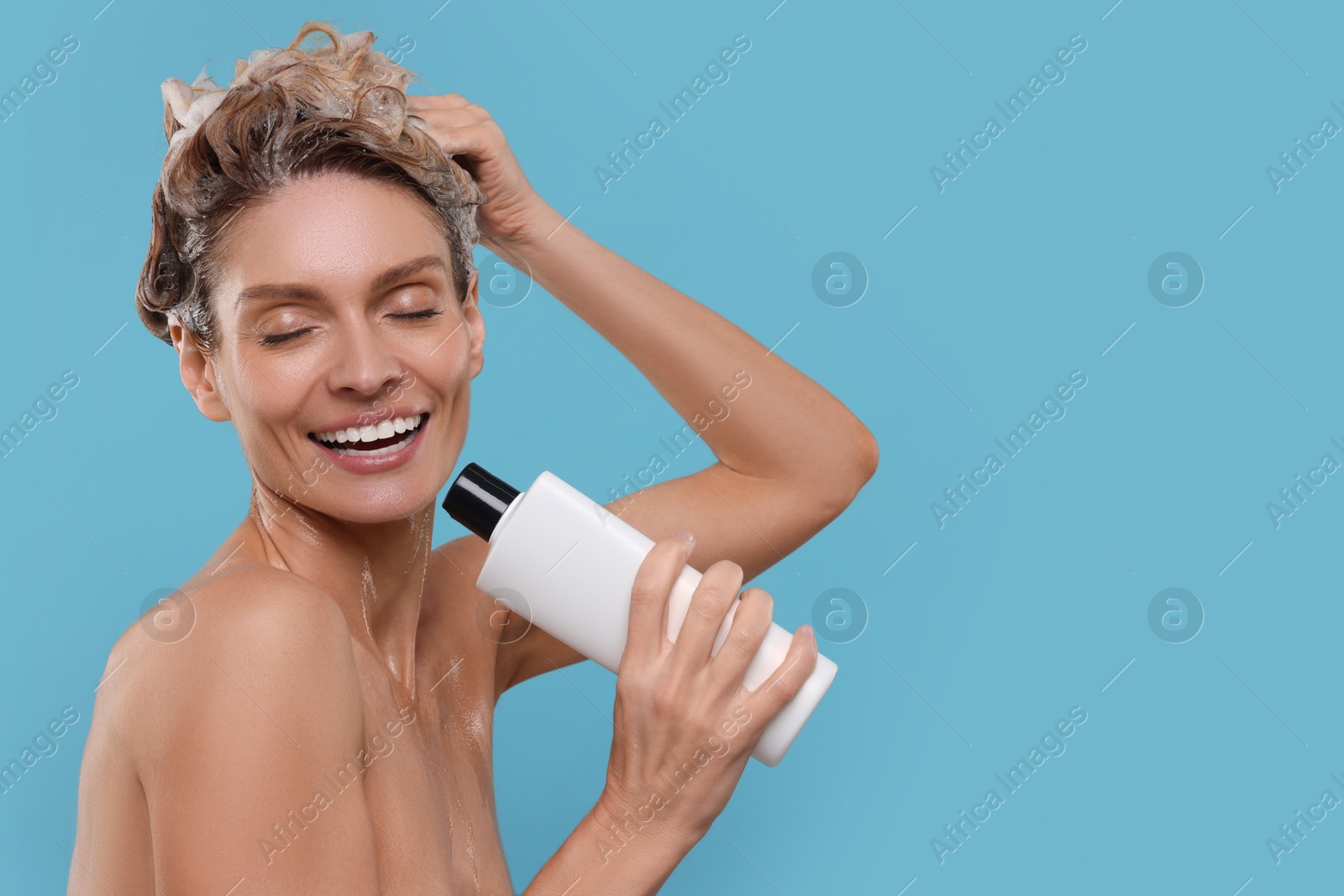 Photo of Portrait of beautiful happy woman with bottle singing while washing hair on light blue background. Space for text