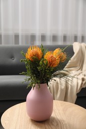 Photo of Vase with beautiful flowers on wooden coffee table near grey sofa indoors