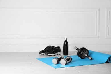 Exercise mat, dumbbells, ab roller, shoes and bottle of water on light wooden floor indoors. Space for text