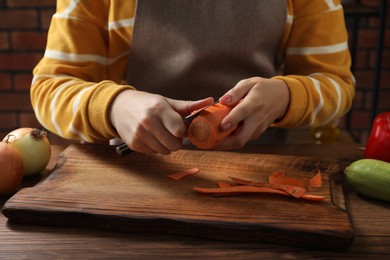 Photo of Woman peeling fresh carrot with knife at wooden table indoors, closeup