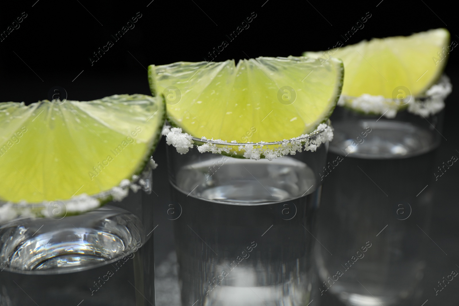 Photo of Mexican Tequila shots, lime slices and salt on table, closeup