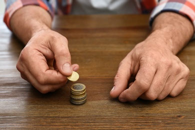 Photo of Senior man stacking up coins at table, closeup