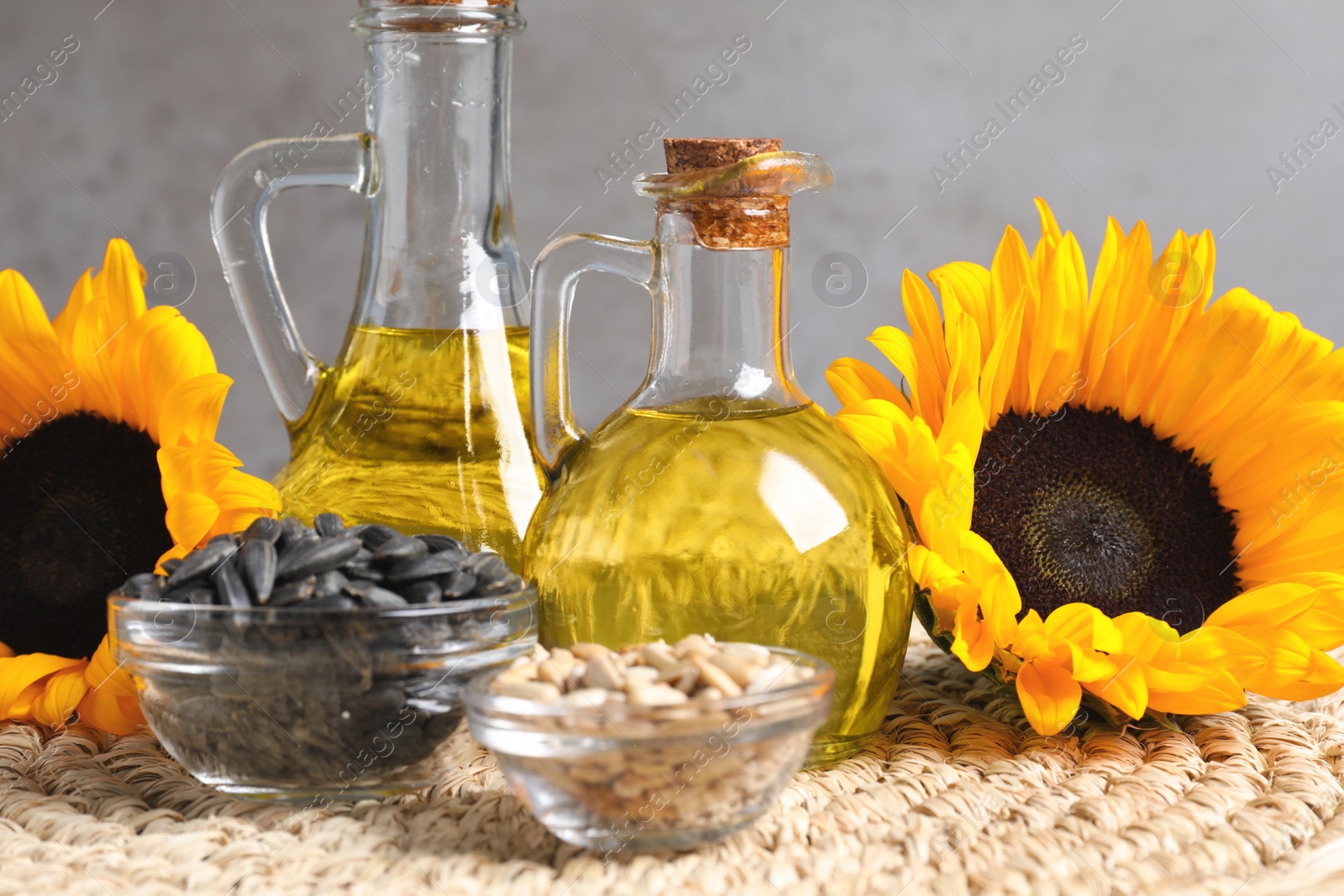 Photo of Sunflower cooking oil, seeds and yellow flowers on wicker mat, closeup