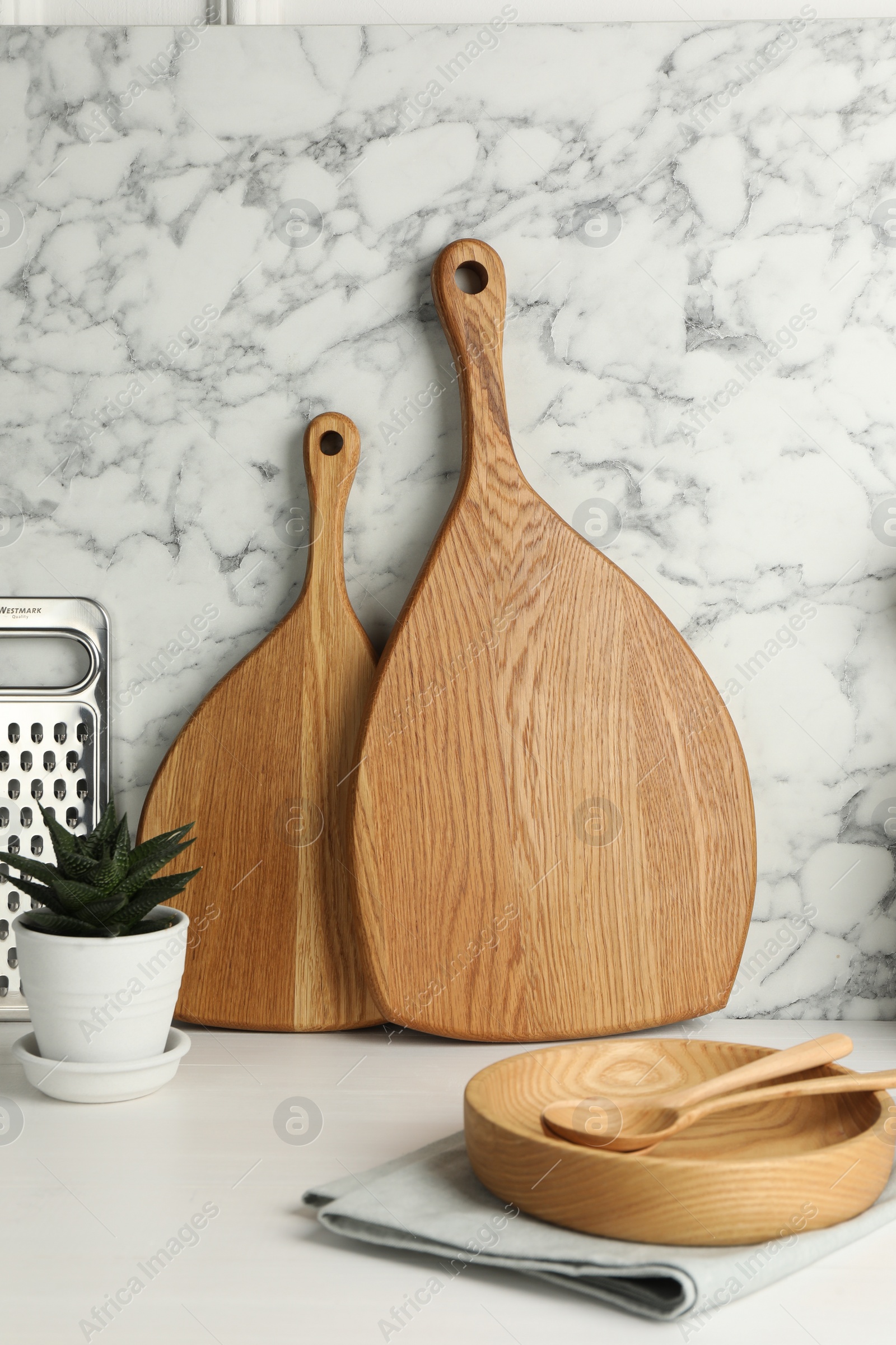 Photo of Wooden cutting boards, plate, spoons and houseplant on white table near marble wall