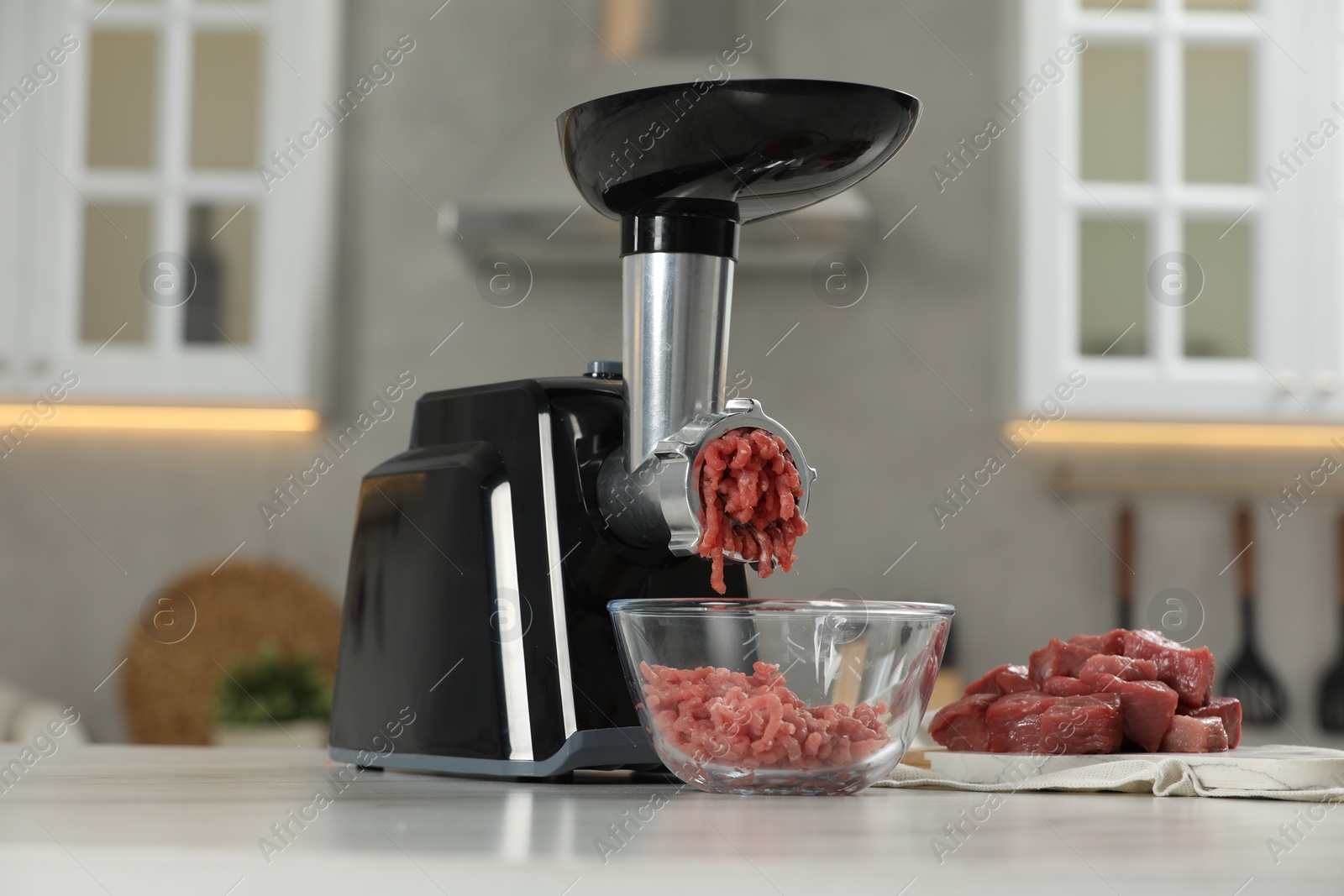 Photo of Electric meat grinder with beef mince on white table in kitchen