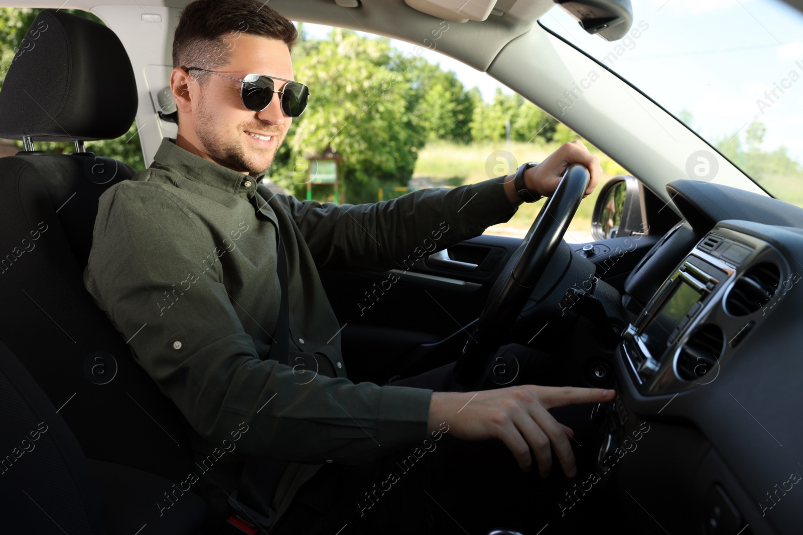 Photo of Choosing favorite radio. Man with sunglasses pressing button on vehicle audio in car