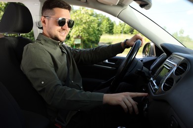 Photo of Choosing favorite radio. Man with sunglasses pressing button on vehicle audio in car