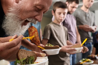 Photo of Senior man with other poor people eating food in charity centre
