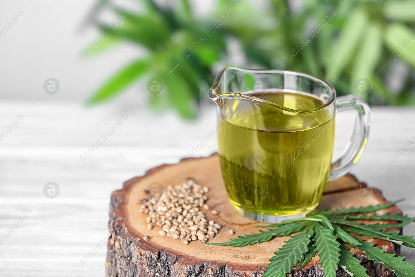 Photo of Jug with hemp oil, seeds and fresh leaves on light table. Space for text