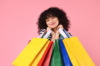 Happy young woman with shopping bags on pink background