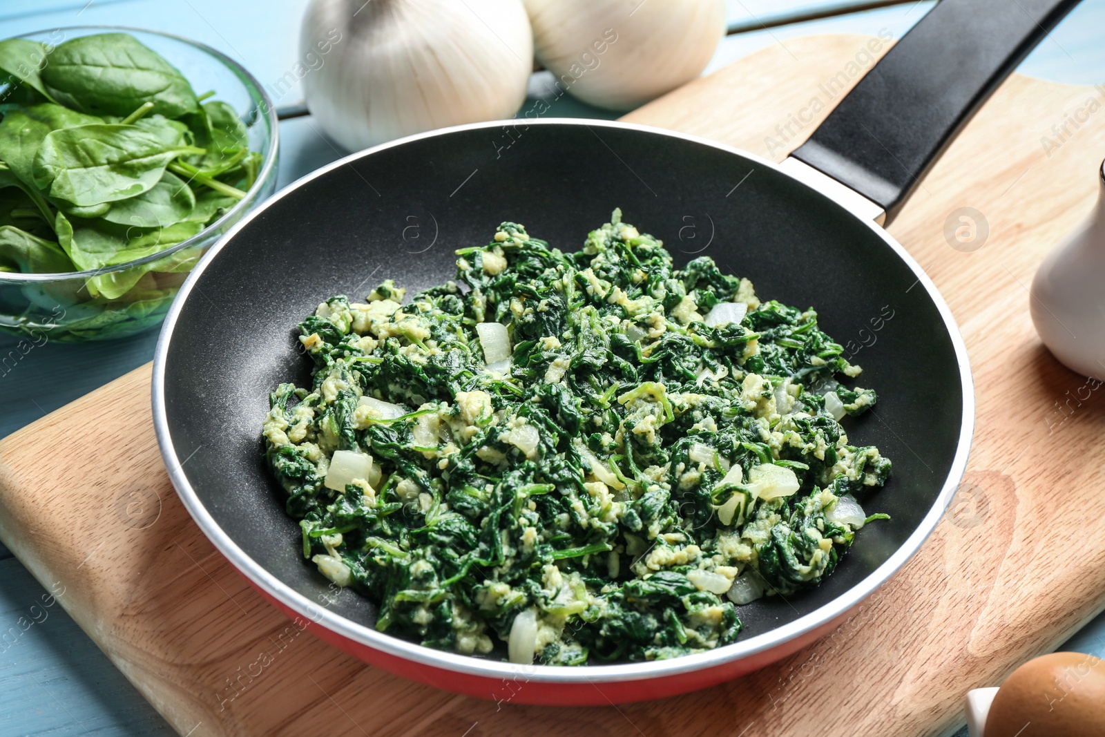 Photo of Tasty spinach in frying pan on light blue table. Healthy food