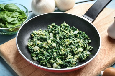 Tasty spinach in frying pan on light blue table. Healthy food