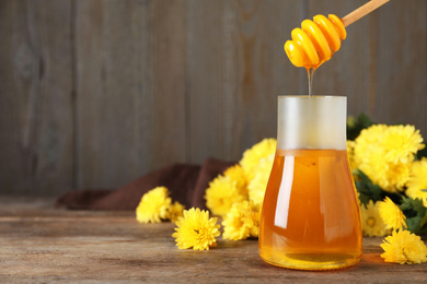 Jar with organic honey and chrysanthemum flowers on wooden table. Space for text