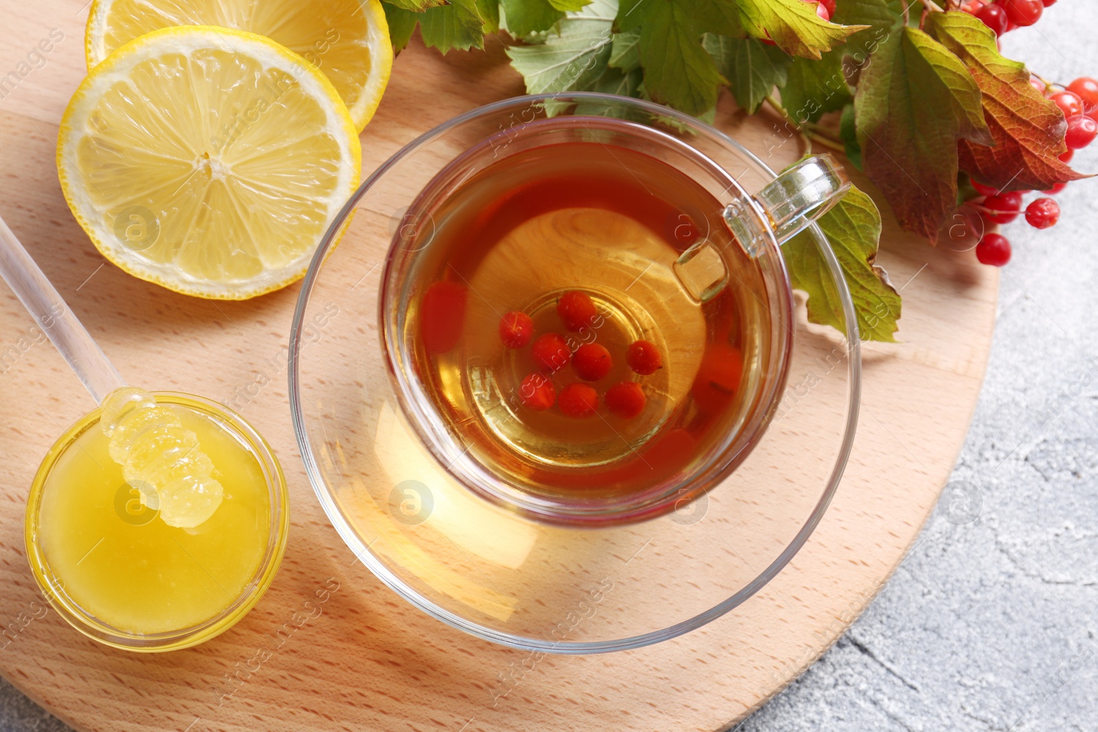 Photo of Cup of delicious tea with lemon, honey and viburnum on light grey table, flat lay