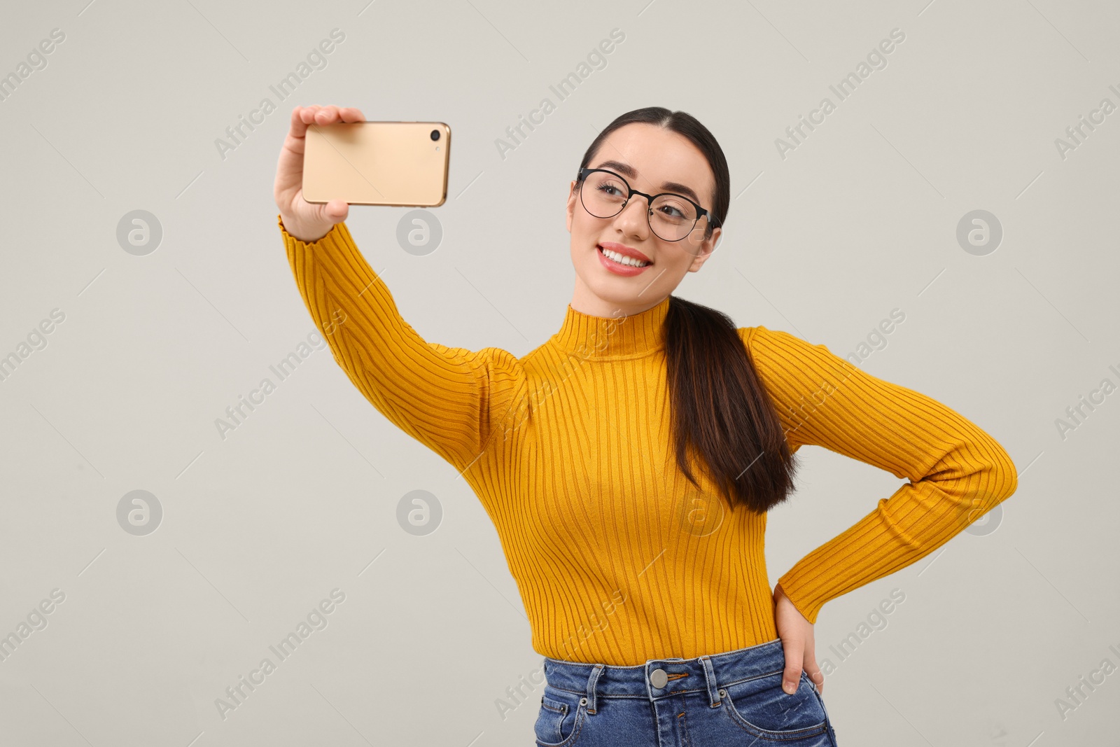 Photo of Smiling young woman taking selfie with smartphone on grey background, space for text