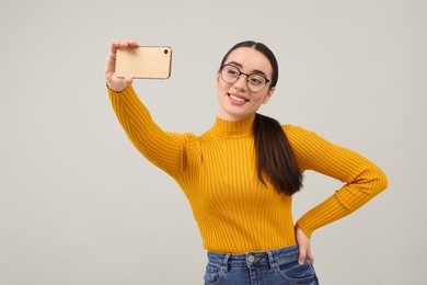 Smiling young woman taking selfie with smartphone on grey background, space for text